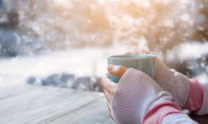 Kvinna värmer sina kalla händer över en kopp varmt te
